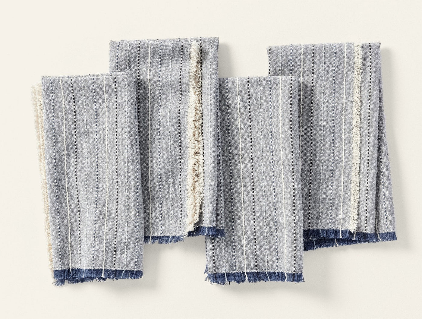 Coyuchi Fringe Stripe napkins fanned flat, showing frayed indigo and ivory fringe edges.