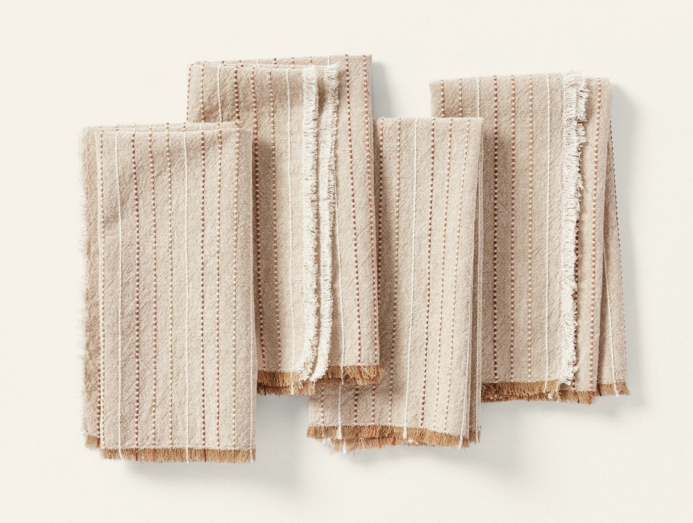 Set of four Coyuchi Fringe Stripe napkins in natural, folded flat, showing striped texture and fringe edges.