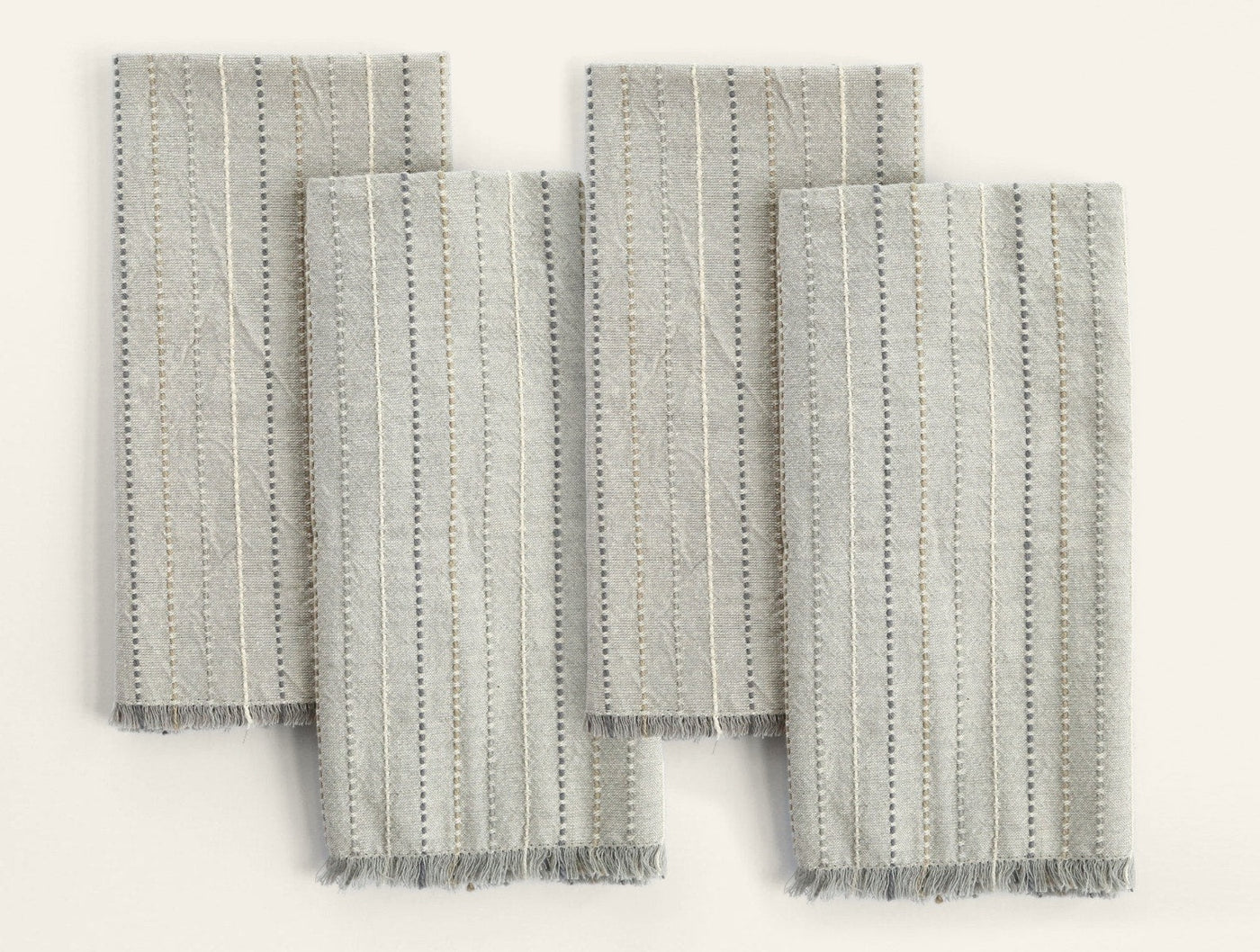 Close-up of four Coyuchi Fringe Stripe napkins in sage, showing dotted stripe weave and frayed hem detail.