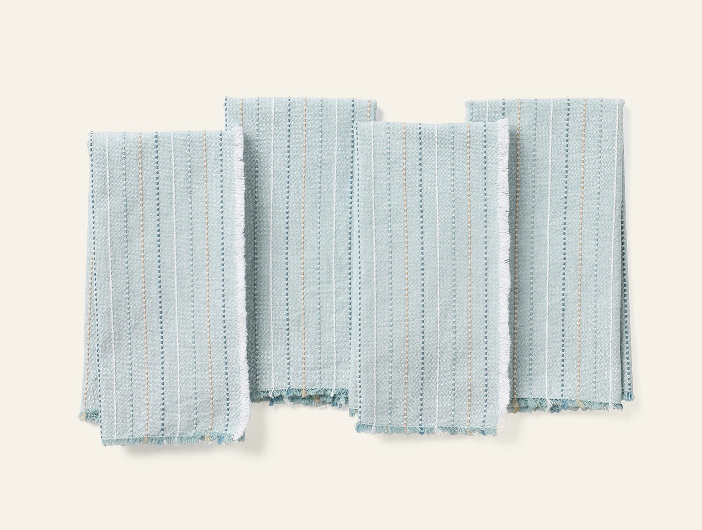 Four Coyuchi Fringe Stripe napkins laid flat, pale aqua with dotted stripe pattern and fringe hem.