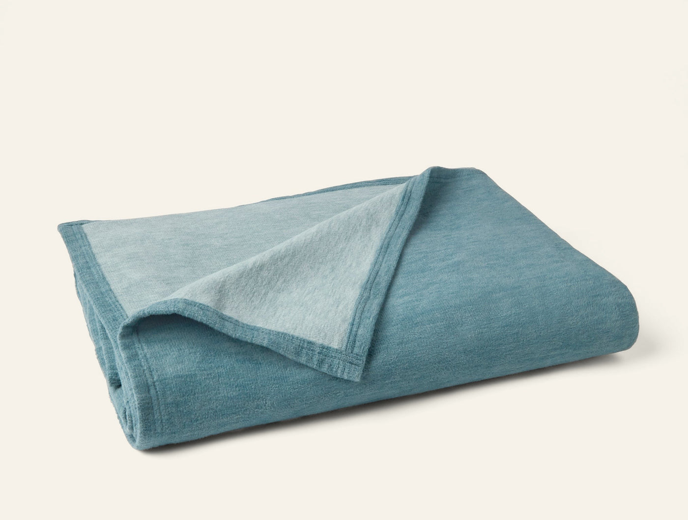 Folded teal cotton blanket showing contrast between deeper exterior and lighter reverse side.