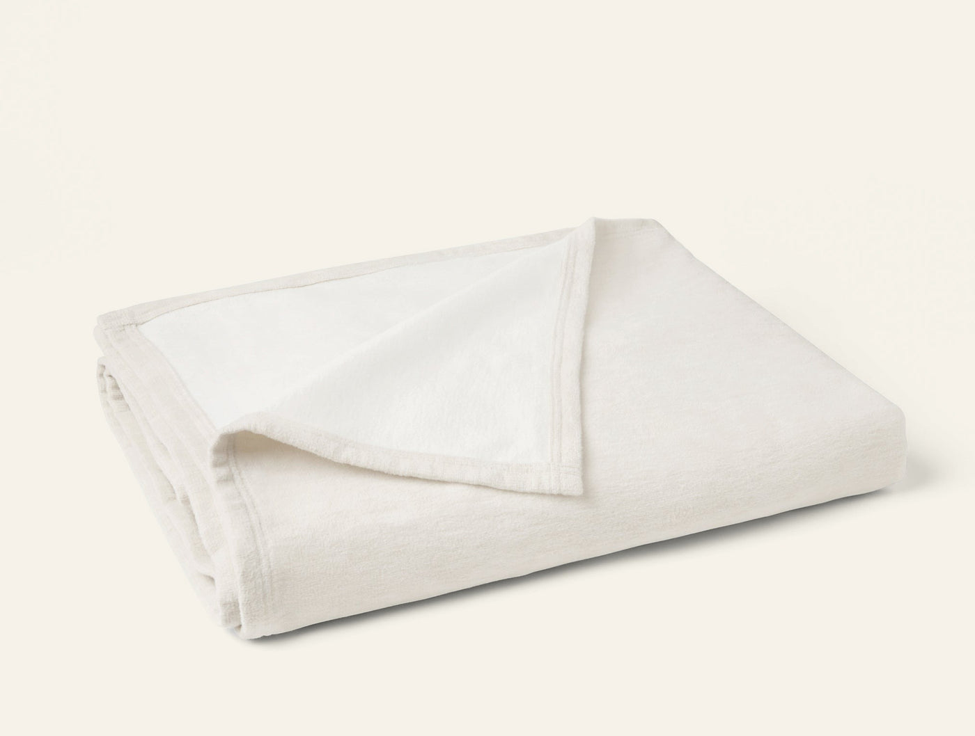 Close-up of ivory folded cotton blanket showing soft stitched border trim detail.