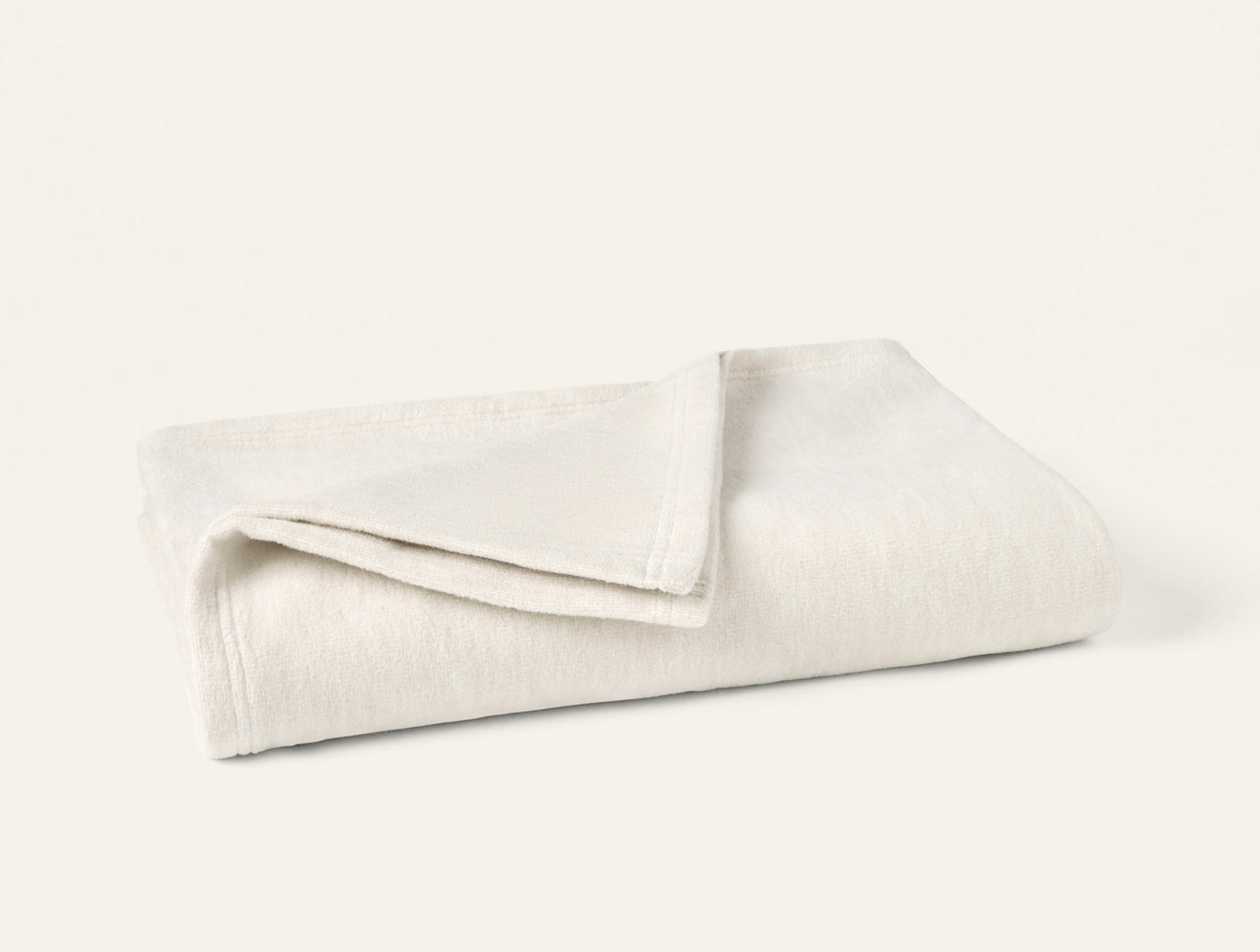 Coyuchi Full Circle Cotton Throw folded, ivory textured weave with subtle ribbed pattern.