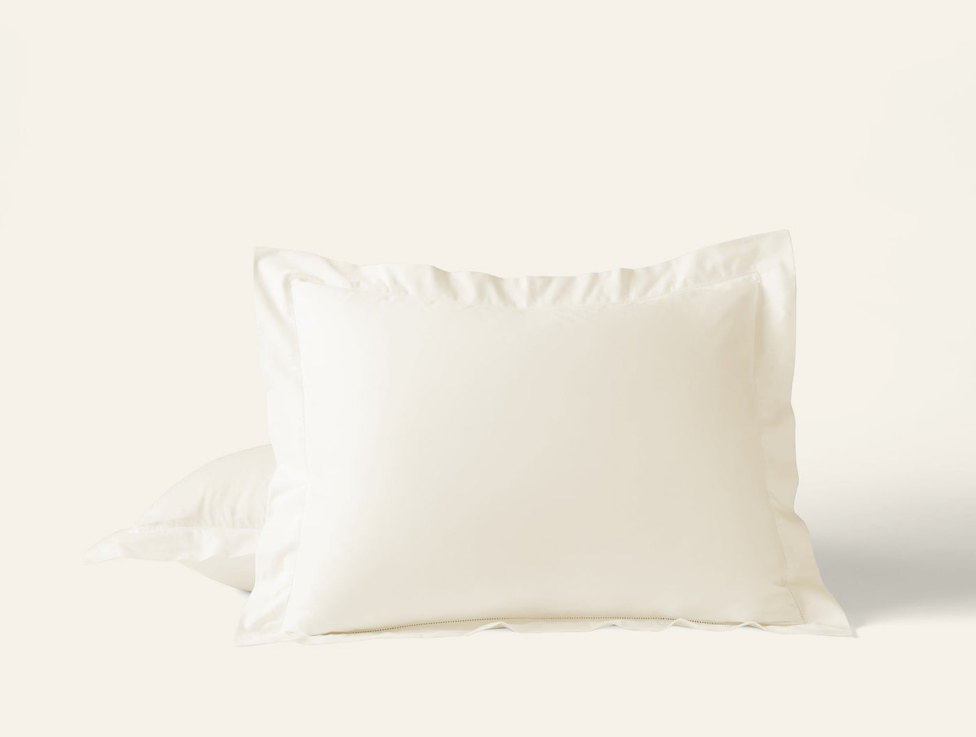 Ivory sateen pillow sham with flange border, slightly gathered fabric visible at base.