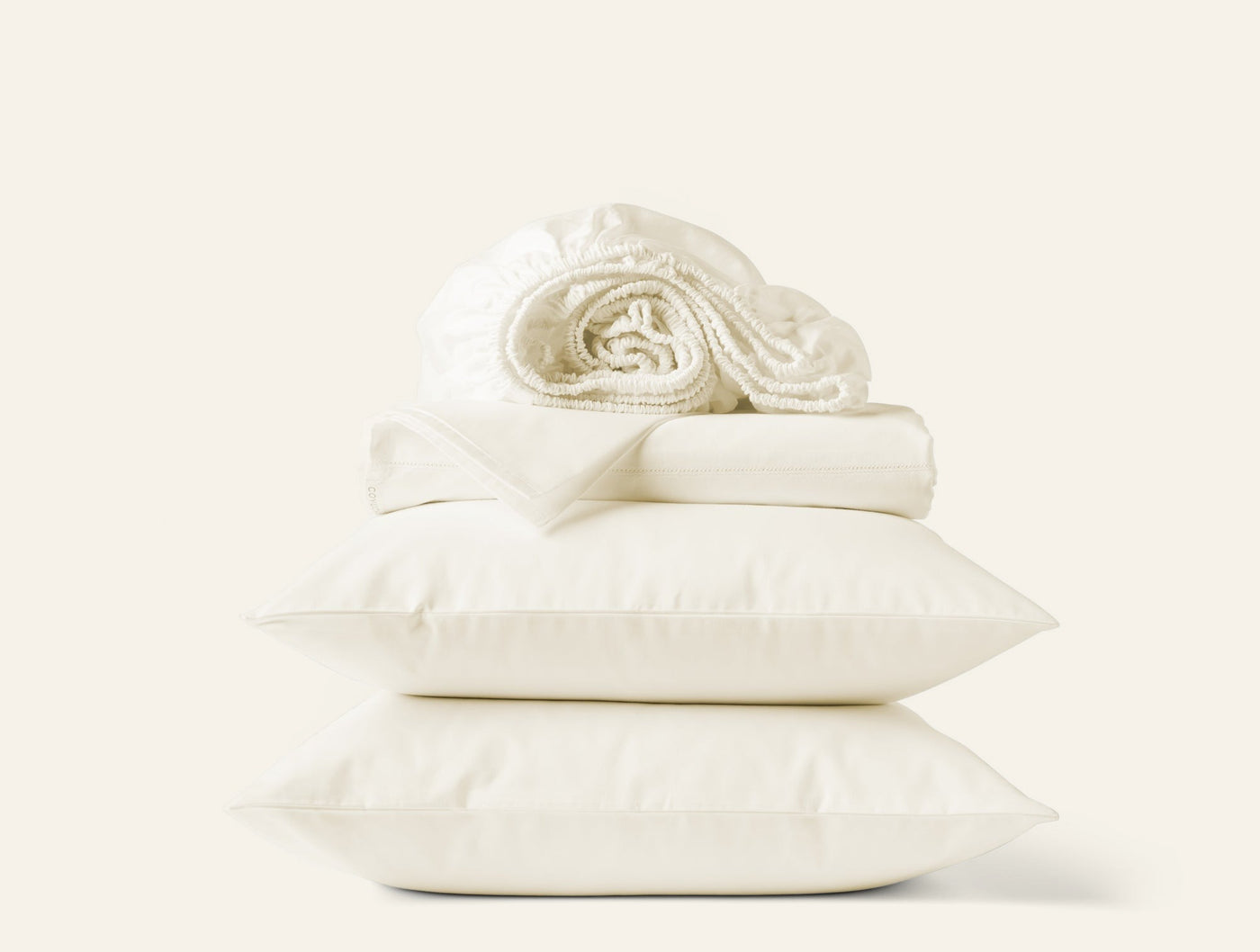 Ivory sateen sheet set stacked with two pillowcases and a rolled fitted sheet on top.