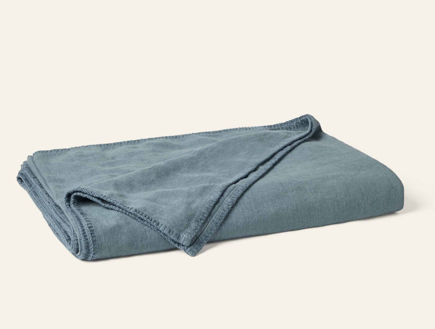 Close-up of folded Coyuchi Helena Linen blanket in slate blue, showing blanket stitch edge trim.