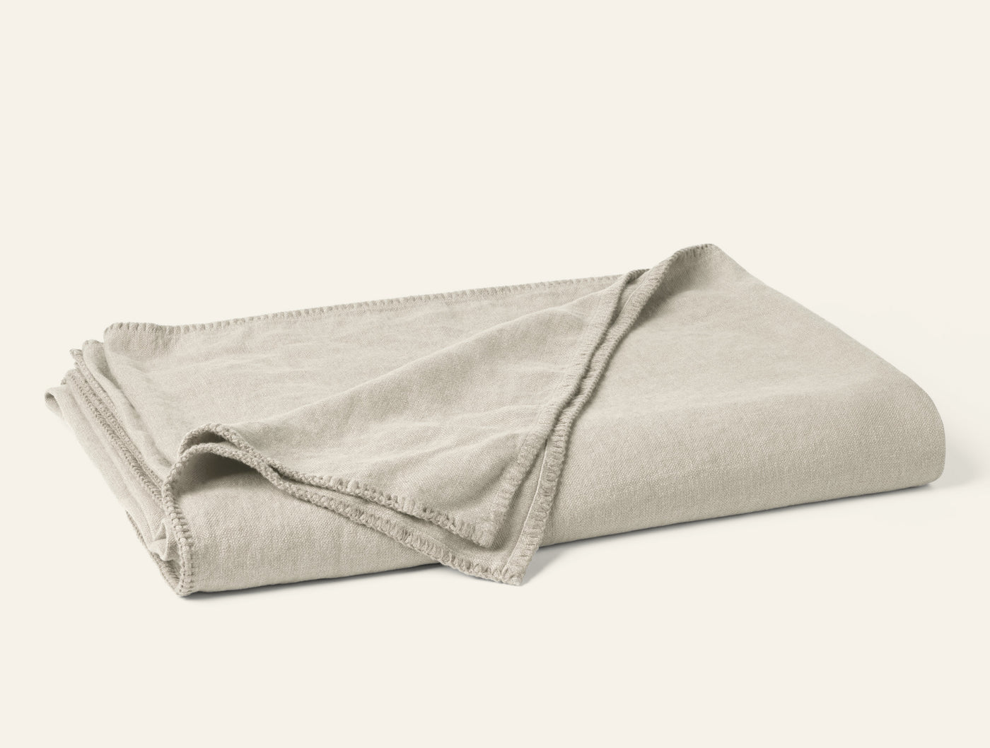 Folded oatmeal linen blanket with contrast blanket-stitch trim detail.