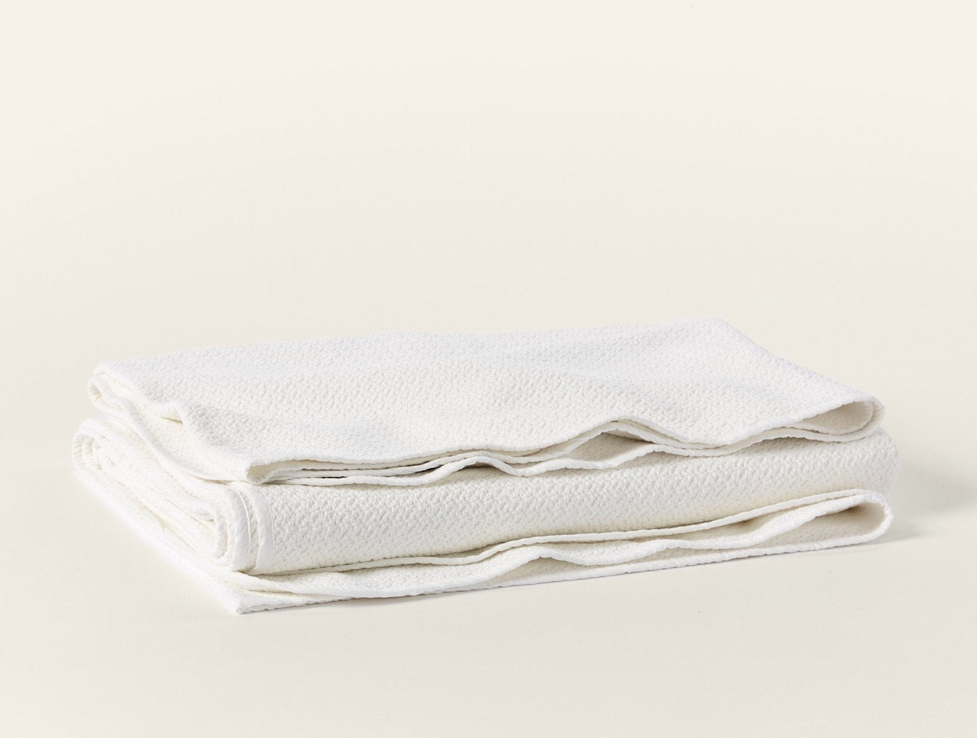 Coyuchi Honeycomb blanket folded, showing ivory textured weave and hemmed edges.