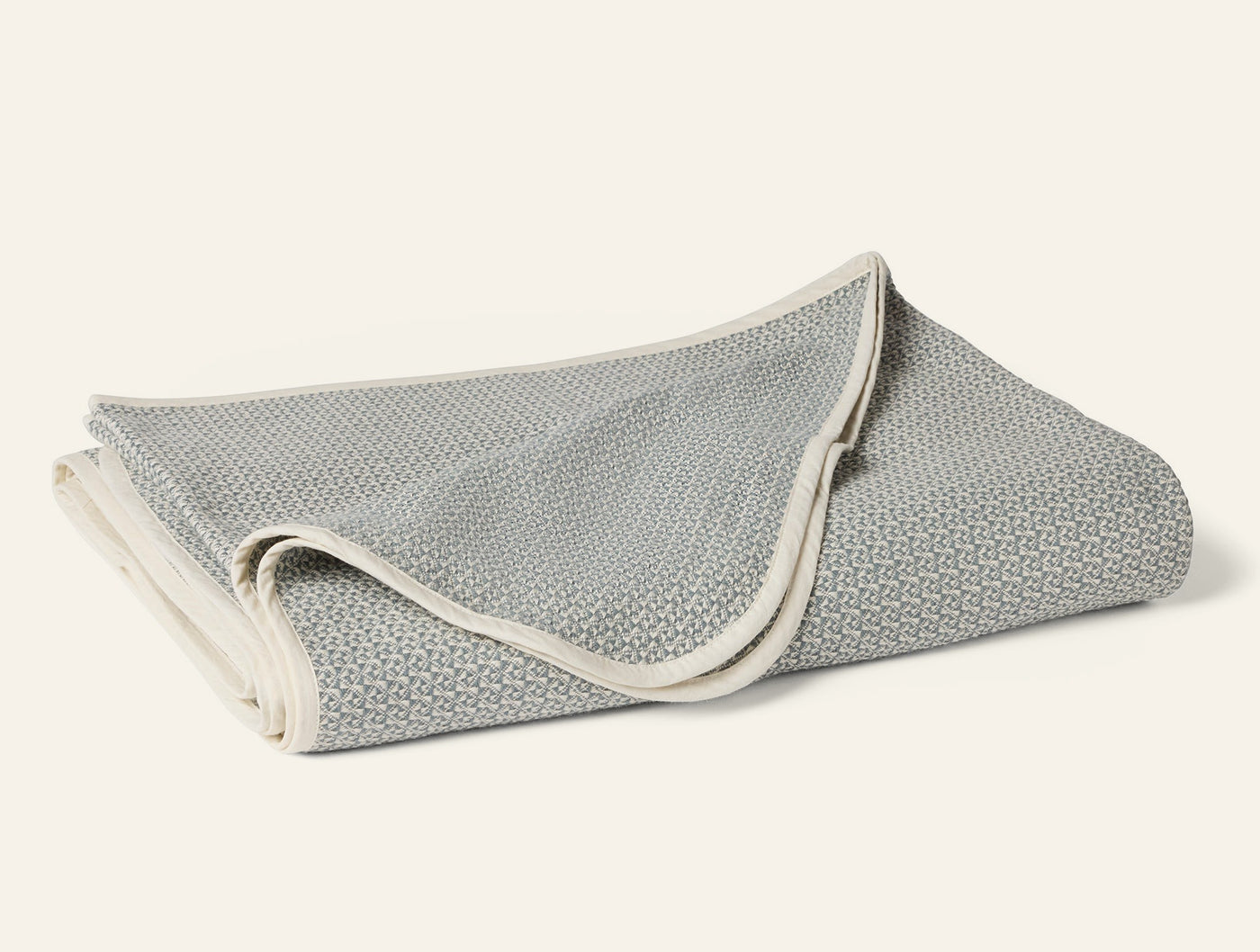 Close-up of folded Coyuchi Honeycomb blanket in sage with ivory binding trim.