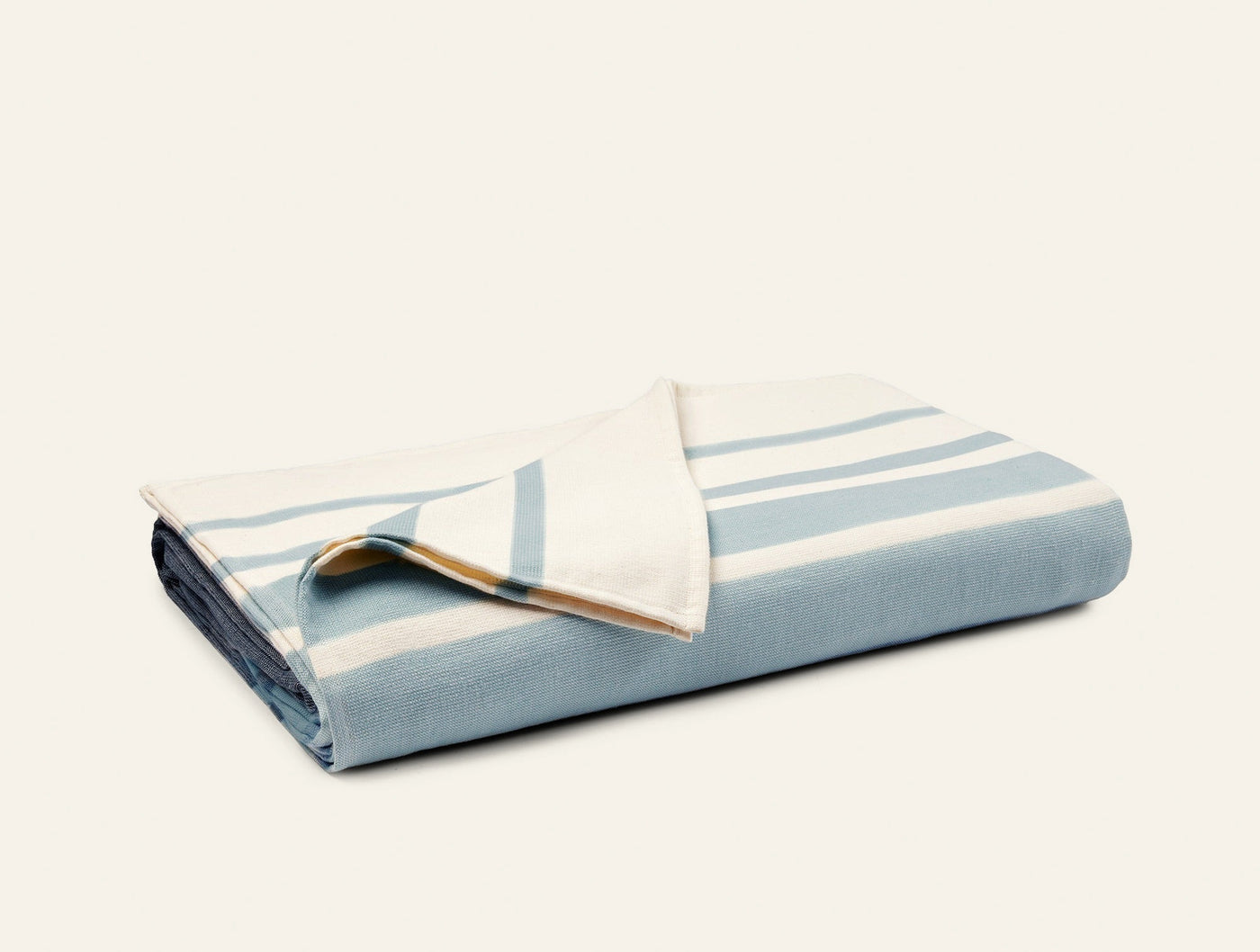 Folded Coyuchi Laguna beach blanket showing pale blue and ivory stripe pattern with corner turned back.