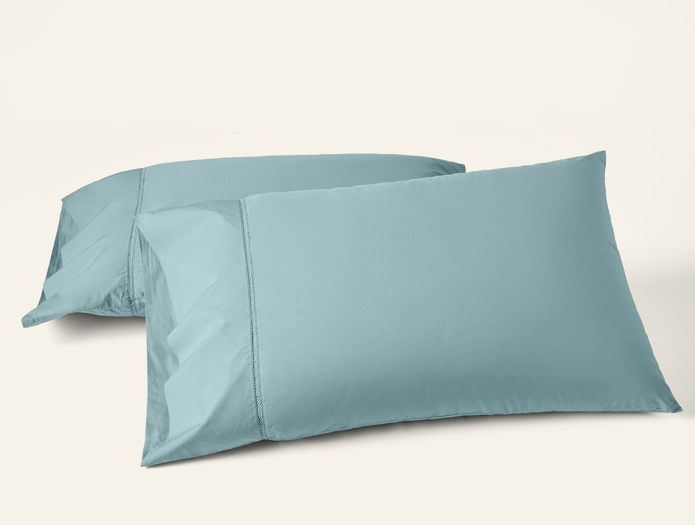 Two Coyuchi Lattice Percale pillowcases in muted teal, stacked at an angle on white background.