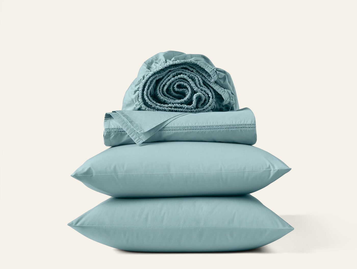 Coyuchi Lattice Percale sheet set stacked with rolled fitted sheet on top, seafoam.