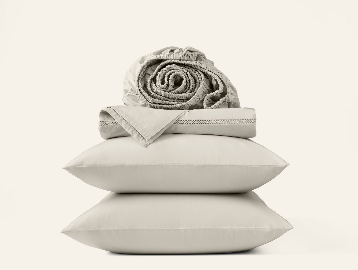 Stacked ivory percale pillowcases with folded flat sheet and rolled fitted sheet on top.