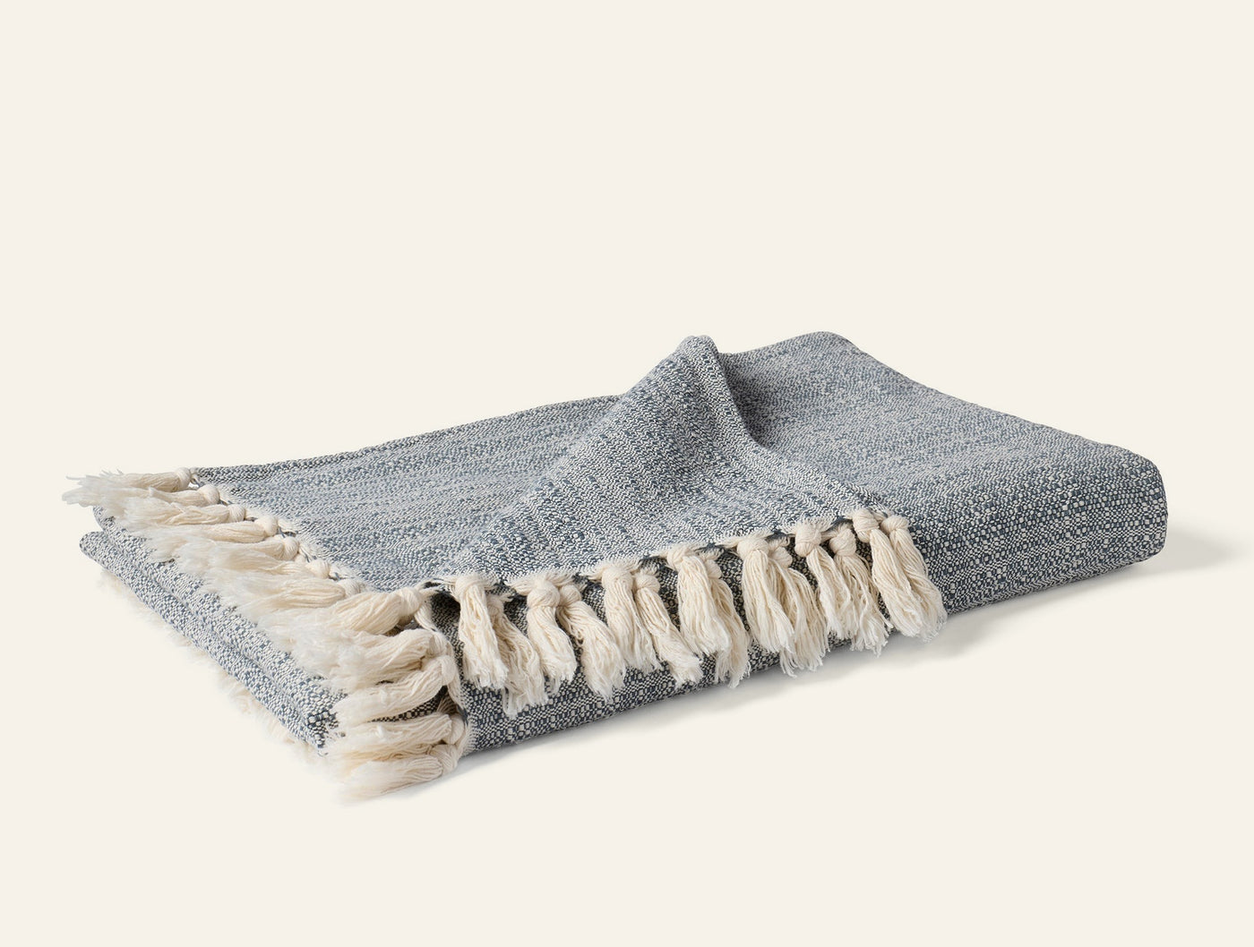 Close-up of Coyuchi Lido throw folded, showing slate woven texture and cream fringe detail.