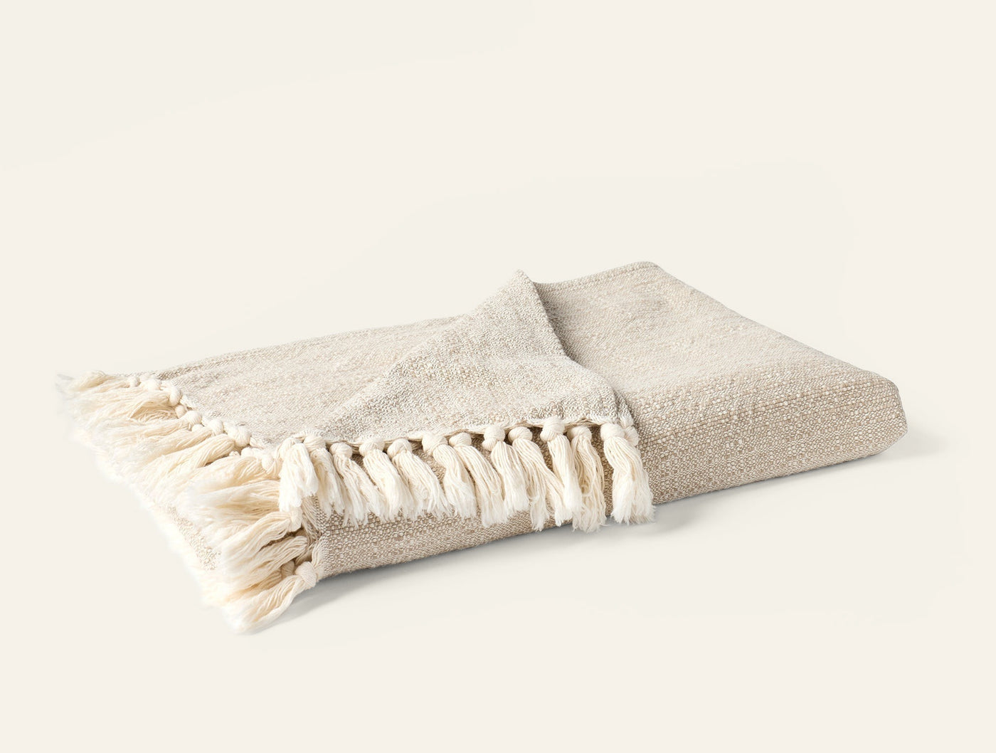 Folded ivory boucle throw with knotted fringe trim, side angle view.
