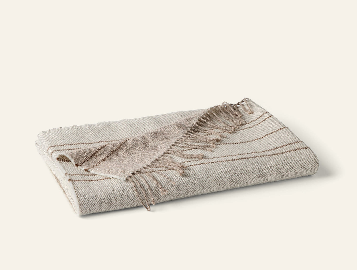 Coyuchi Lima Reversible Alpaca Throw folded, ivory with tan stripe detail and fringe trim.