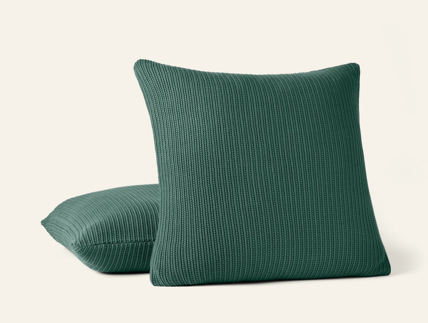 Two Coyuchi Linea Knit pillows in forest green with ribbed texture, stacked against white background.