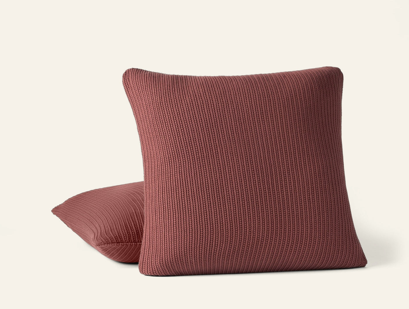 Two Coyuchi Linea Knit pillows in terracotta, ribbed texture, stacked on white background.