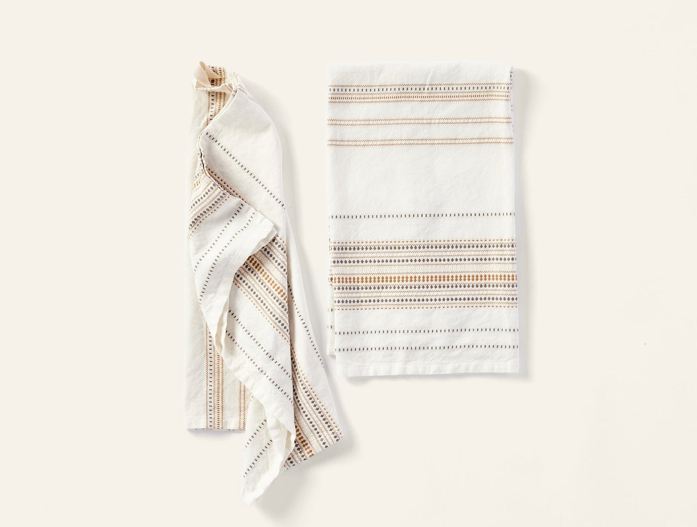 Coyuchi Lobos hand towel pair, one folded flat, one draped, ivory with multicolor stripe detail.
