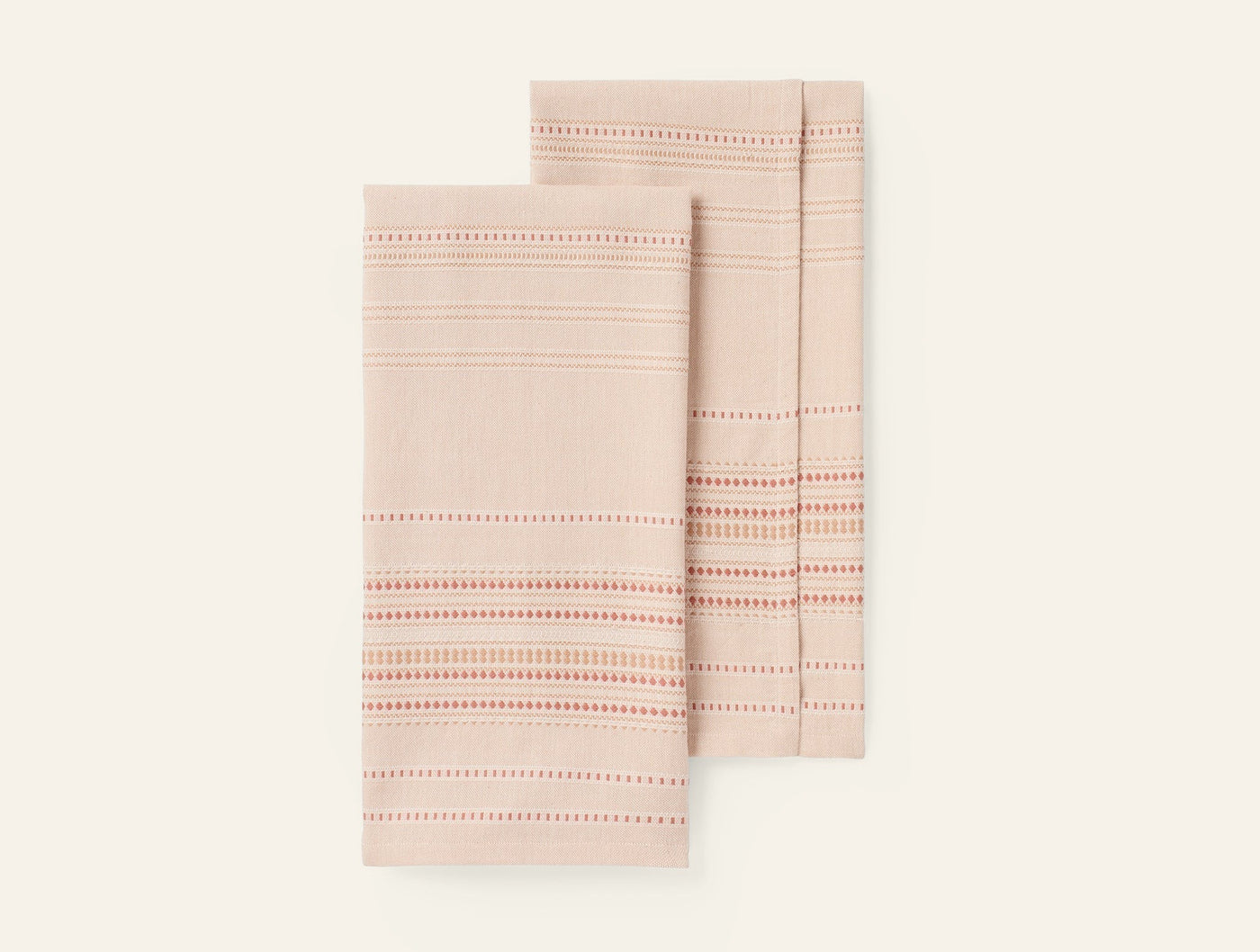 Pair of Coyuchi Lobos hand towels showing coral and red dotted stripe detail on blush linen.