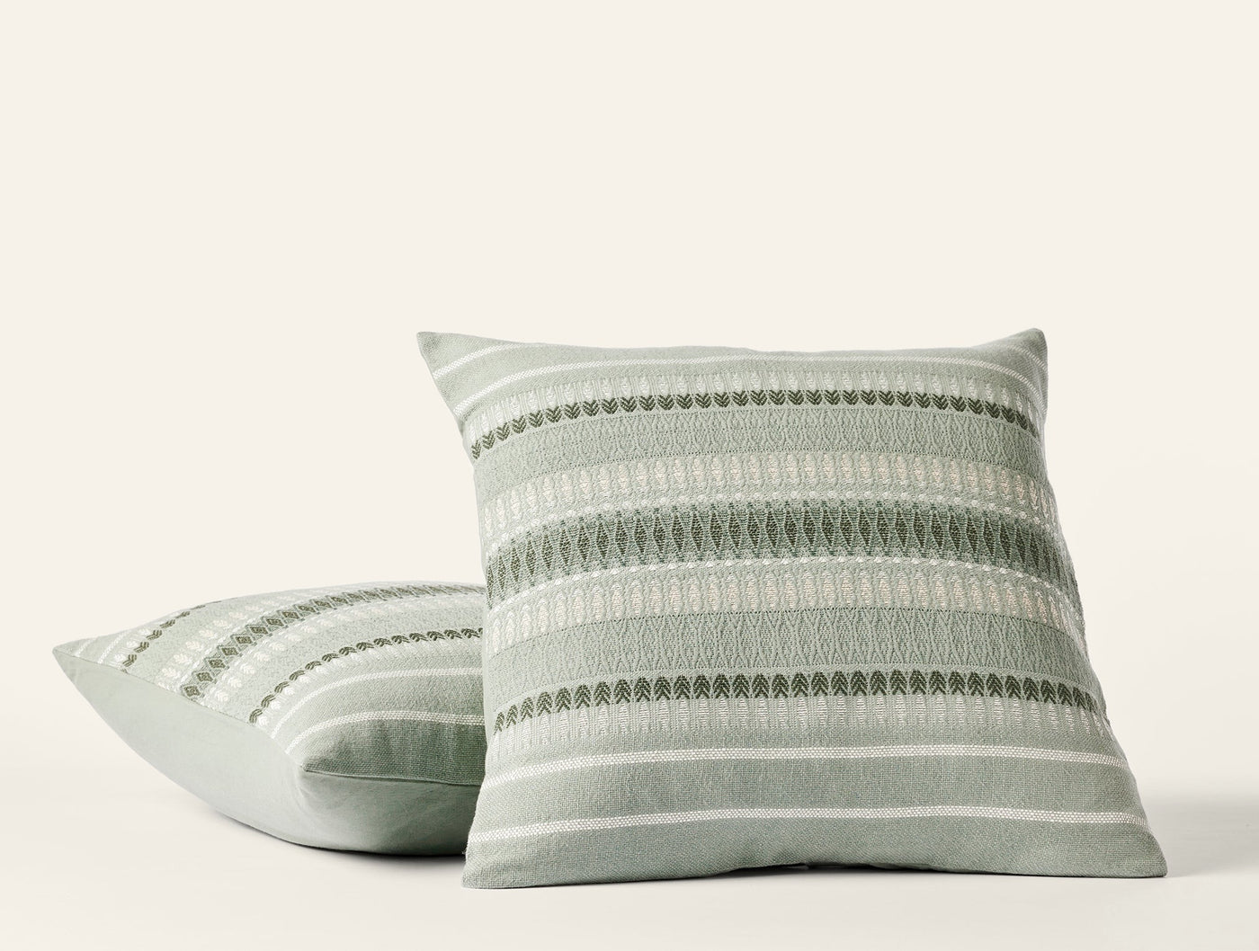Two Coyuchi Lost Coast pillows in sage, woven stripe and dot pattern, white background.