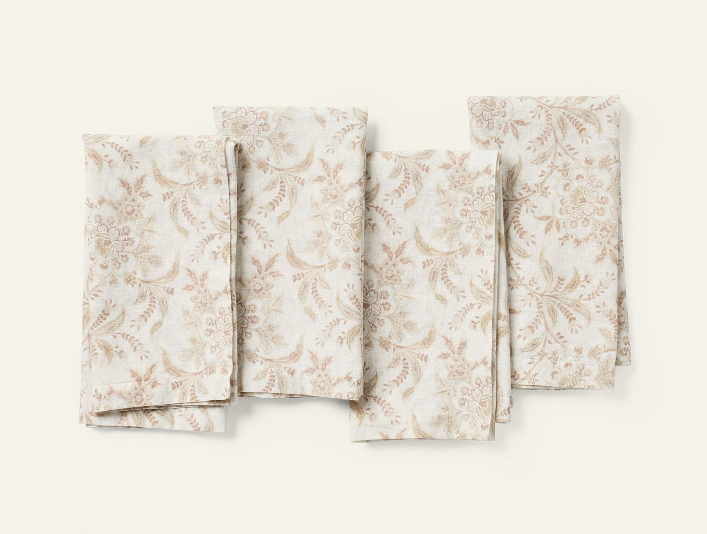 Four folded Coyuchi Marguerite napkins with taupe floral print on ivory linen, flat lay.