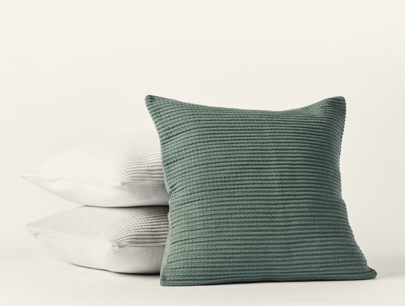 Three Coyuchi Marshall pillows stacked in sage, natural, and white with ribbed texture.