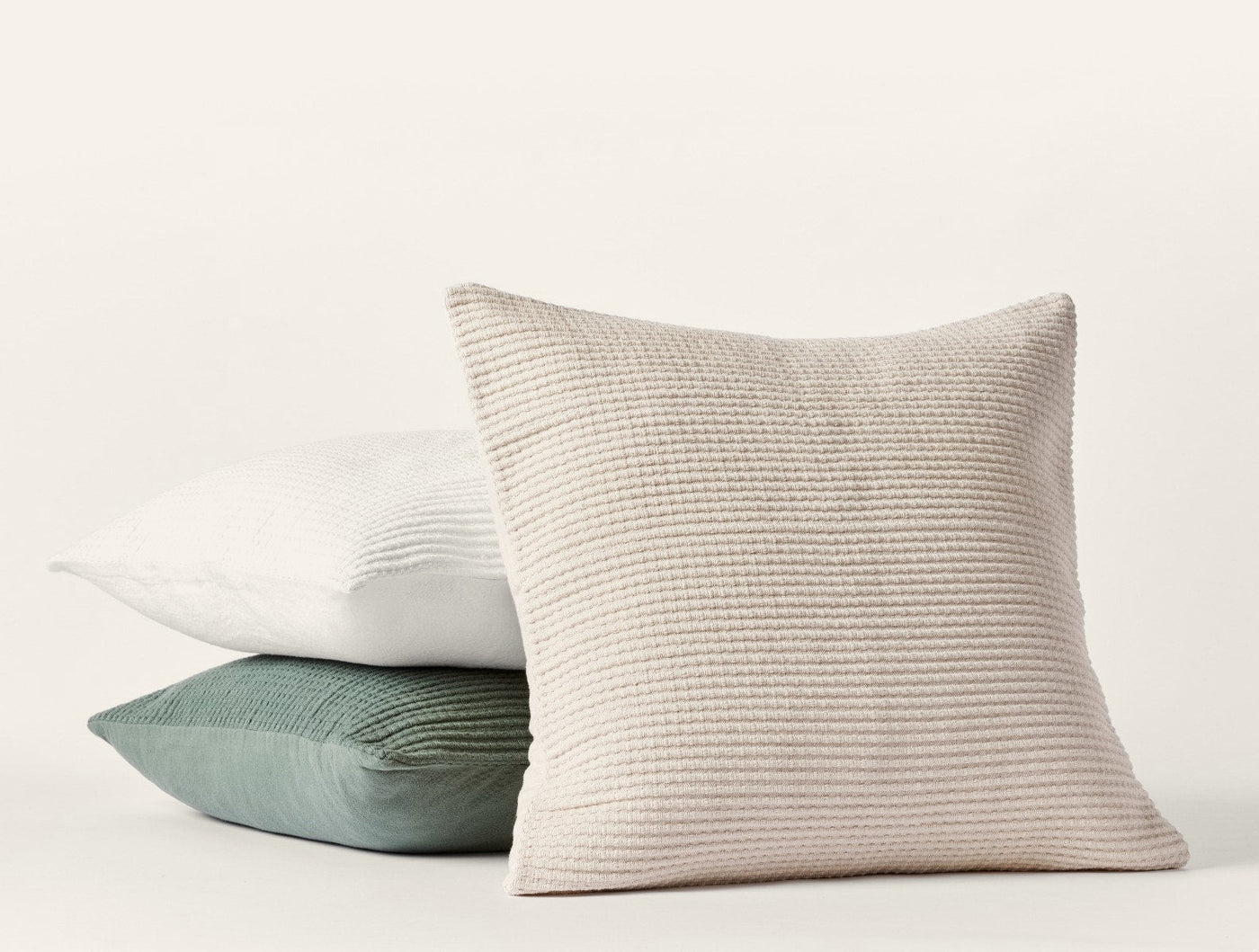 Three stacked Coyuchi Marshall pillow covers in ivory, white, and sage green showing textured weave detail.