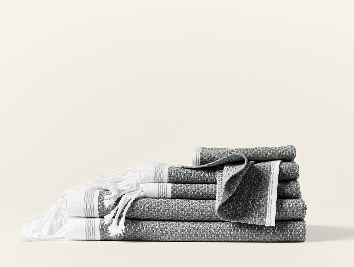 Slate grey waffle-weave towel set with white fringe and stripe trim, stacked and folded.