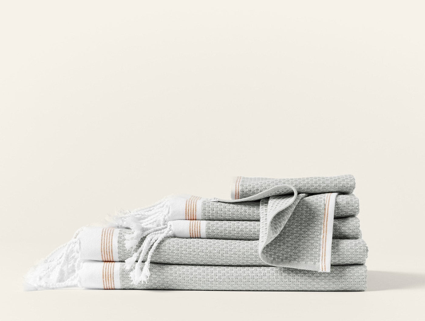Stacked sage waffle-weave towels with fringe and terracotta stripe trim on white background.