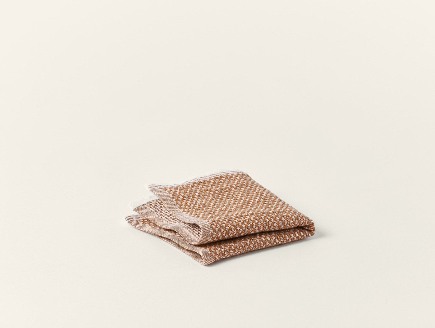 Close-up of two folded Coyuchi Mediterranean guest towels in warm terracotta woven texture.