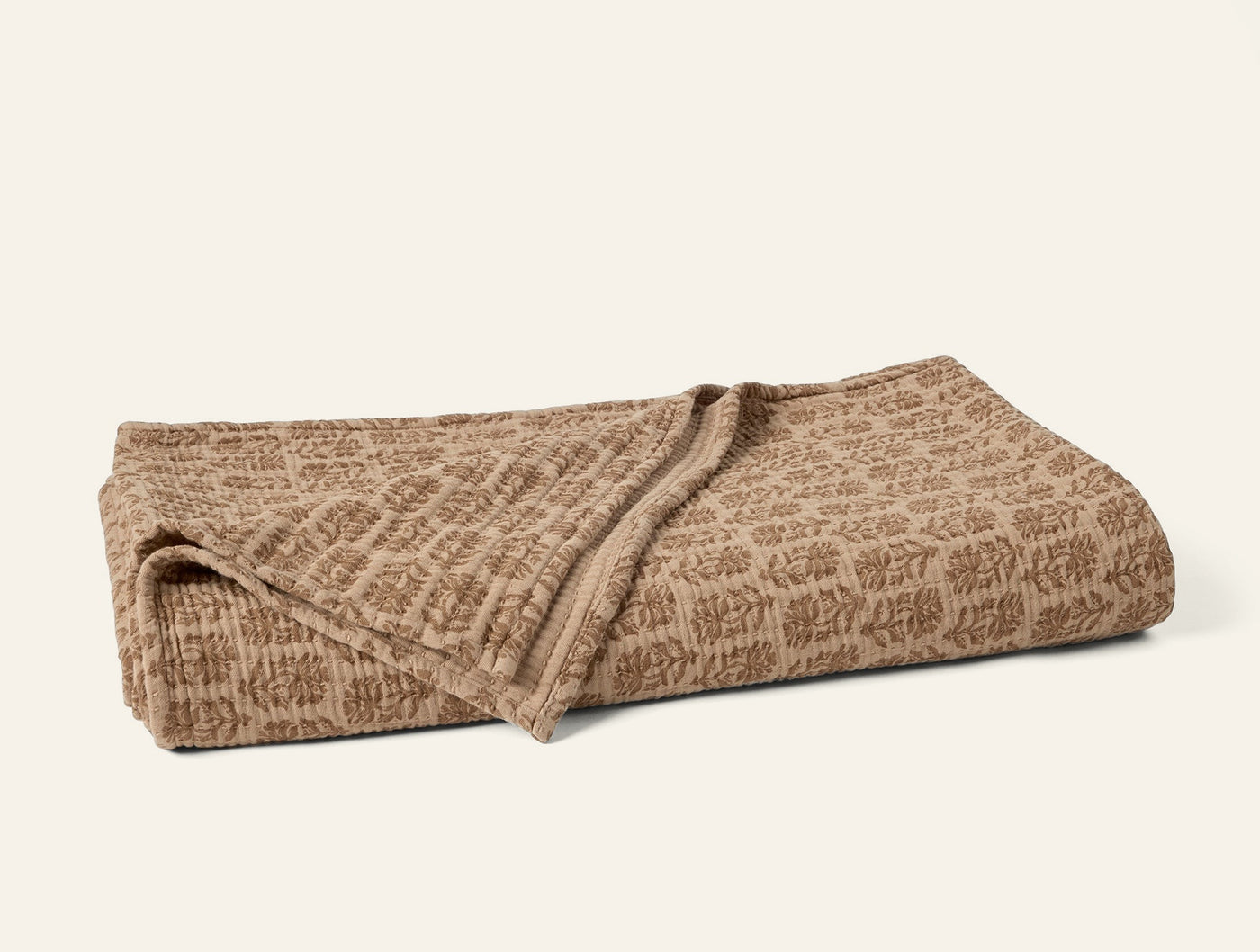 Coyuchi Mirada Matelasse blanket in camel, folded to show textured floral jacquard weave.
