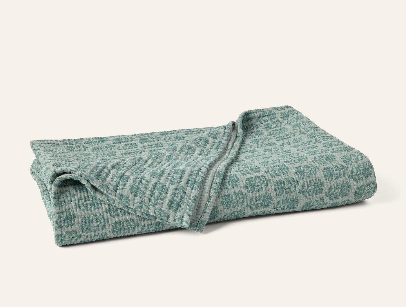 Folded sage green matelassé blanket showing botanical jacquard pattern and texture.
