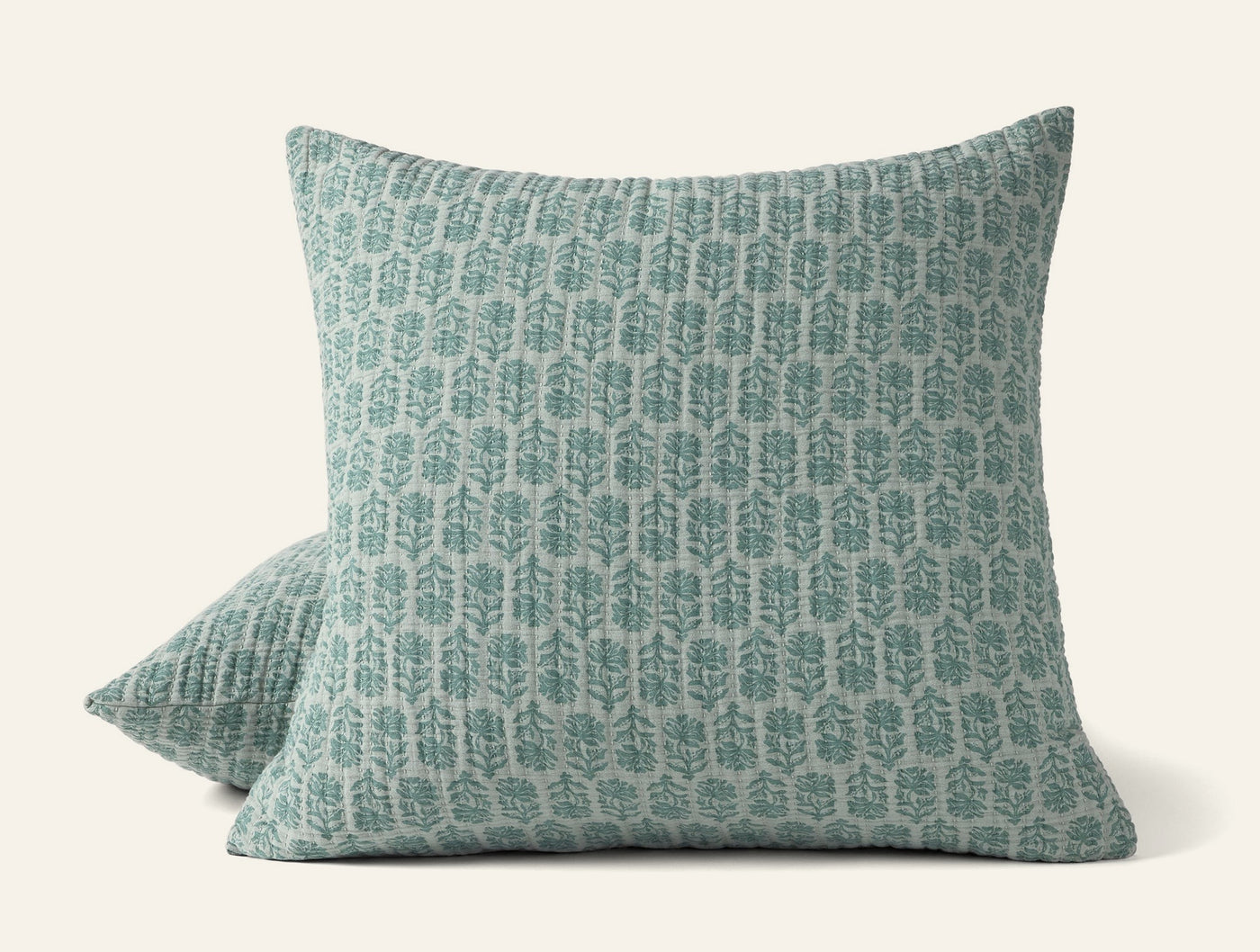 Close-up of two Coyuchi Mirada Matelassé shams in sage with block-print botanical motif.