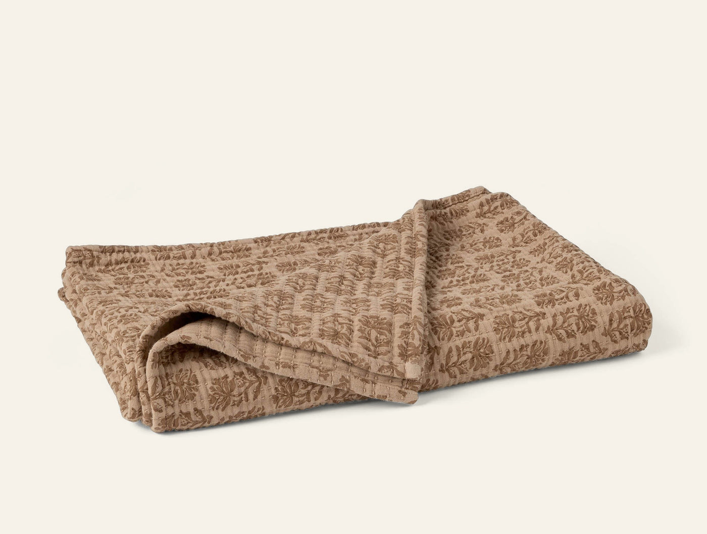 Coyuchi Mirada Matelasse throw in camel with tonal botanical block-print pattern, folded.