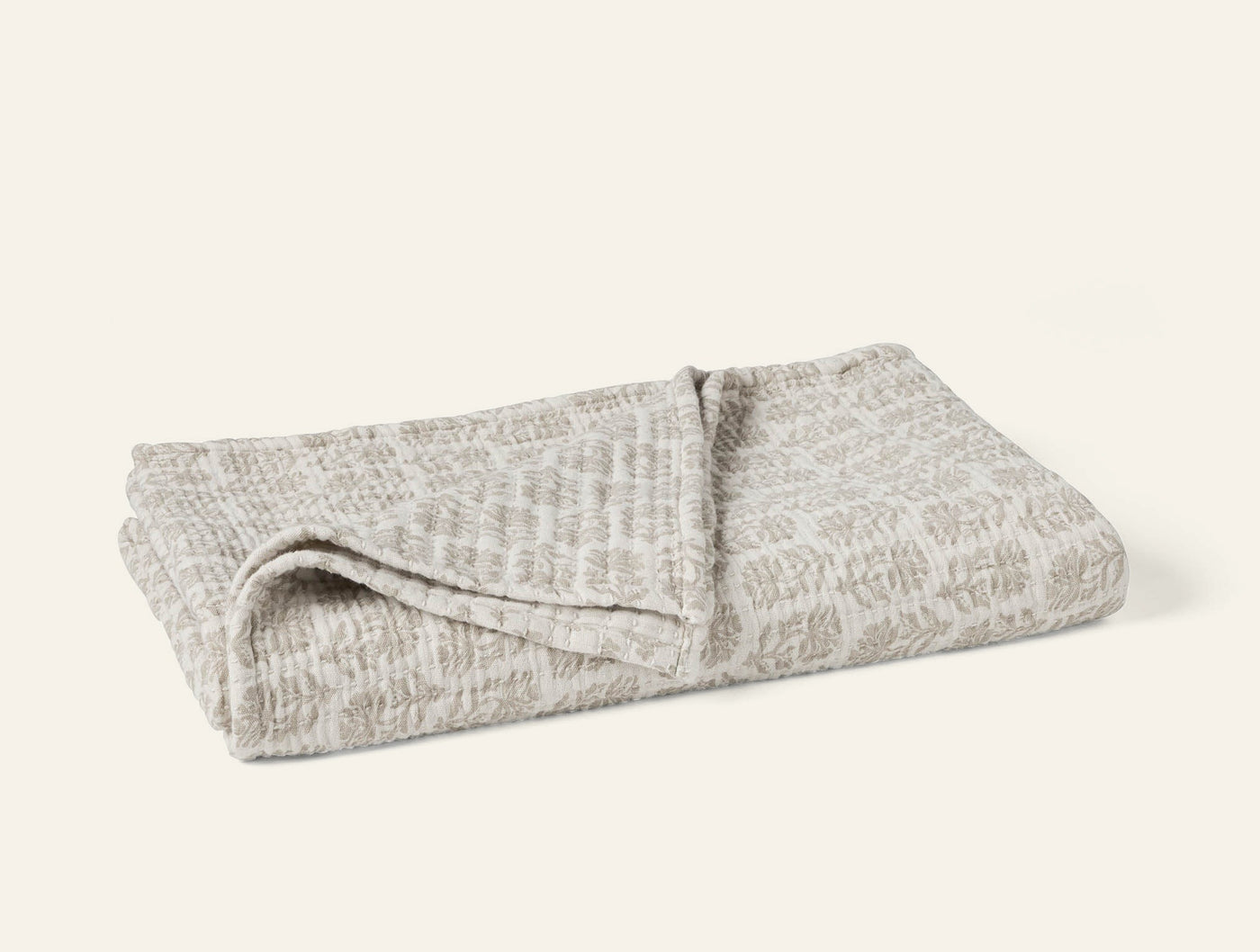 Folded Coyuchi Mirada Matelassé throw in natural, showing allover woven pattern on top surface.
