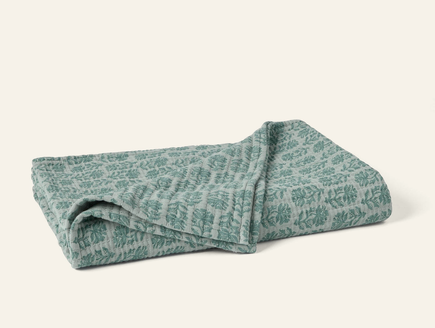 Folded sage green Coyuchi Mirada Matelasse throw with tonal botanical pattern.