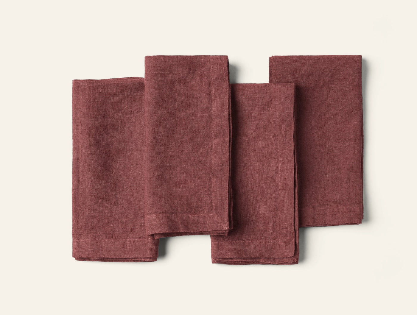 Four folded dusty rose linen napkins fanned out on a white surface.