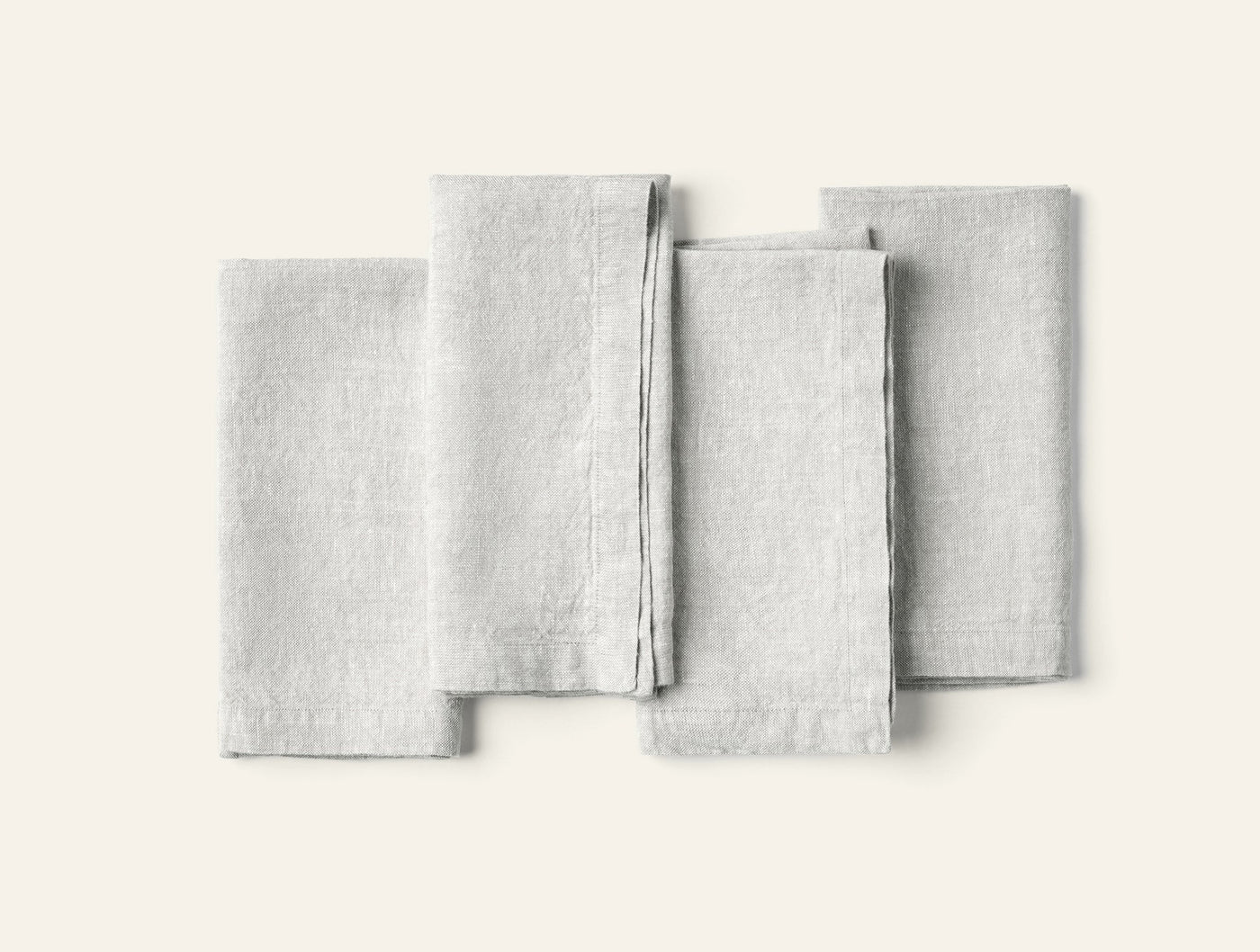Four folded Coyuchi Mojave Linen napkins fanned flat on white background, pale grey.