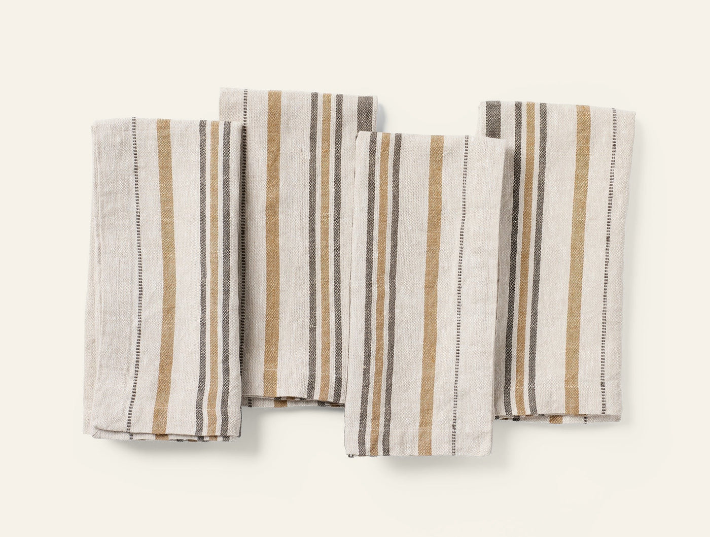 Four Coyuchi Mojave Linen napkins fanned flat, showing ochre and slate multi-stripe weave.