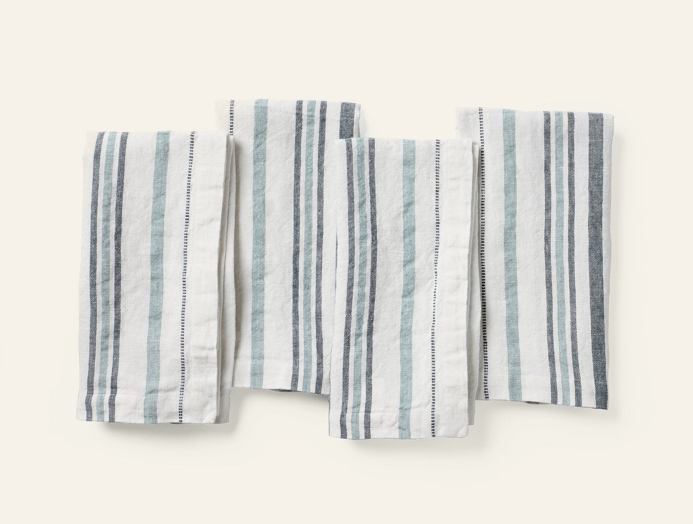 Four folded Coyuchi Mojave linen napkins in ivory with blue and grey stripes, flat lay view.