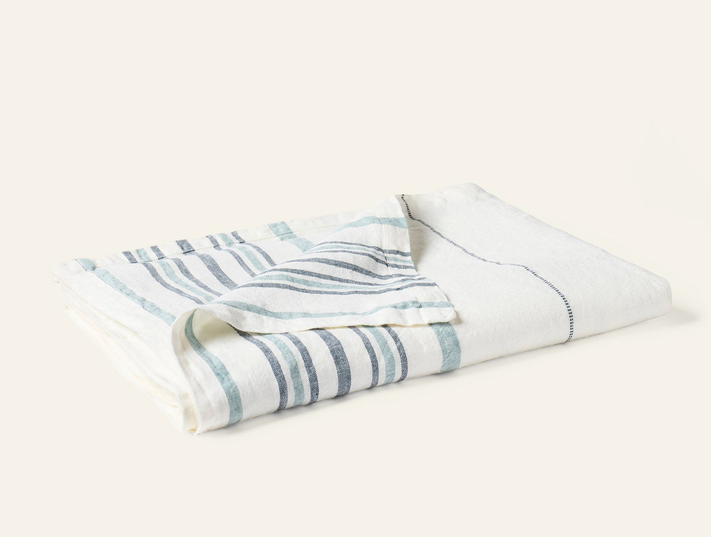 Folded ivory linen throw with varied-width slate and seafoam stripes, angled view.