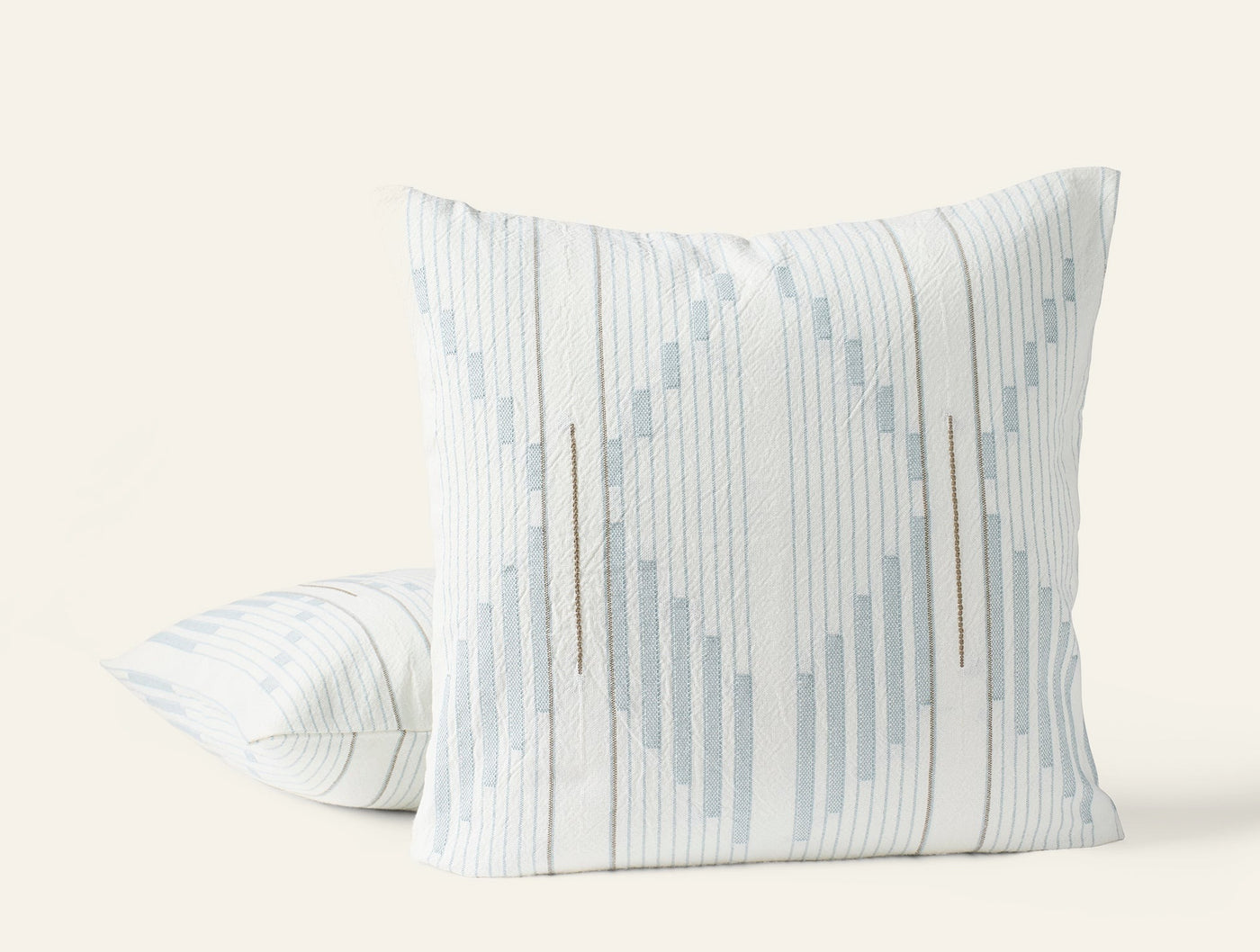 Two Coyuchi Morelia pillows, ivory with pale blue geometric stripe pattern, angled view.