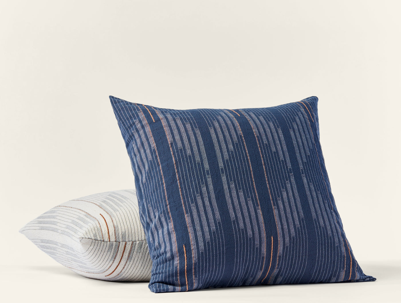 Close-up of navy Coyuchi Morelia sham with copper stripe detail, ivory striped sham beside it.