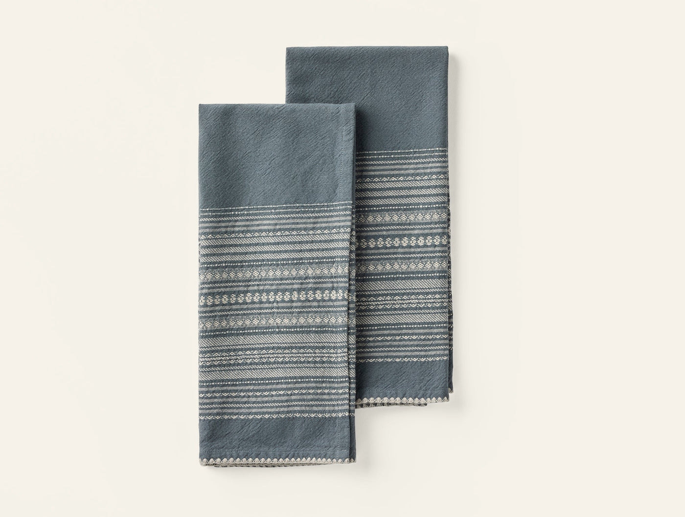 Two folded Coyuchi Oak hand towels in slate blue with woven stripe border detail.