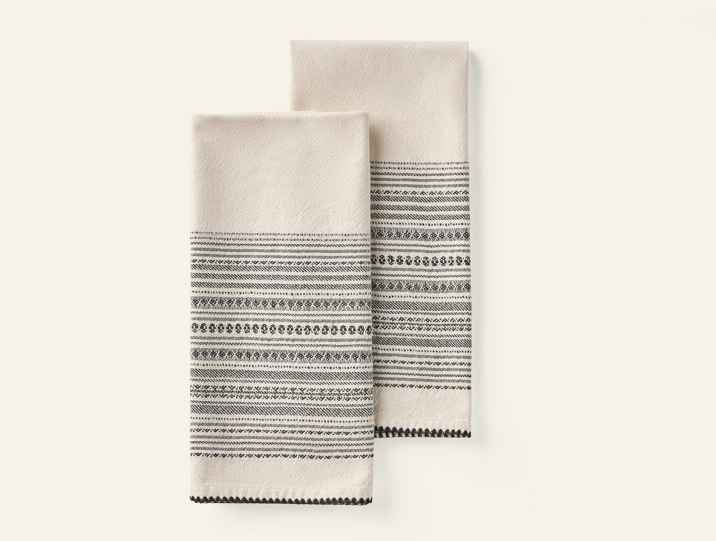 Close-up of two folded Coyuchi Oak hand towels in ivory with dark charcoal woven stripe border detail.