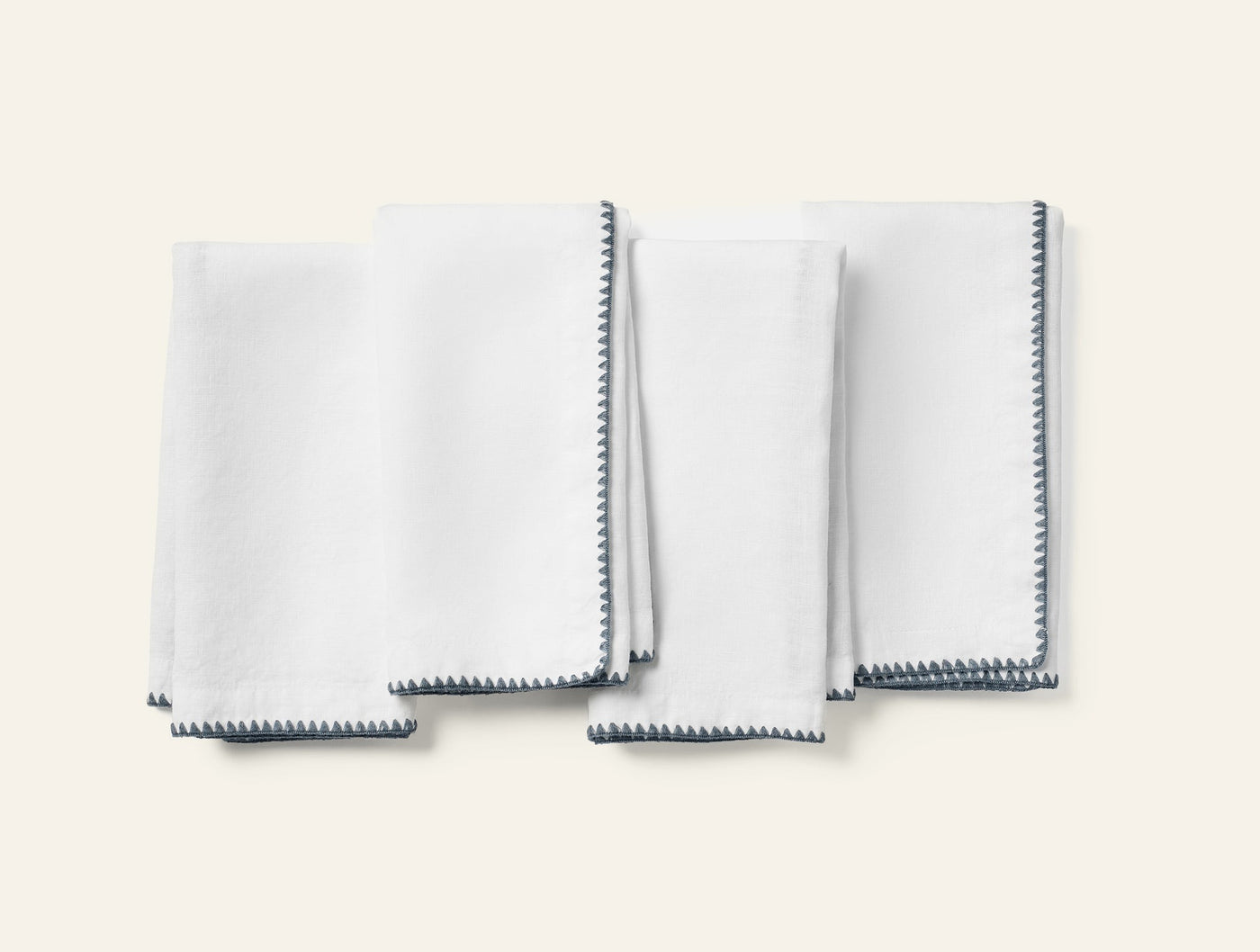 Close-up of four white linen cocktail napkins with charcoal crochet-edge trim, folded flat.