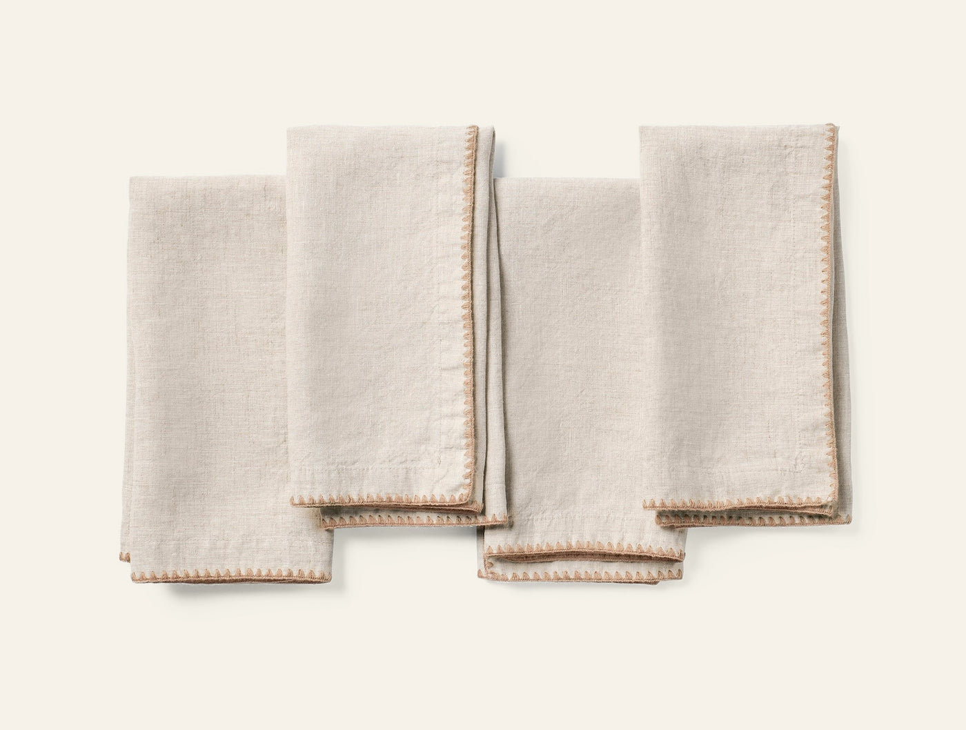 Four natural linen napkins folded flat, showing tan embroidered picot edge trim.