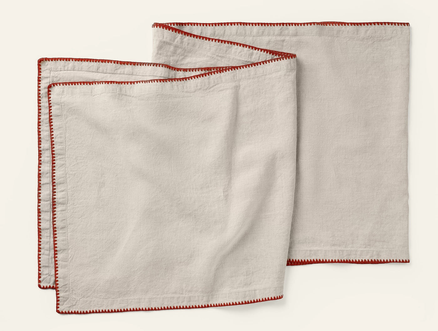 Three ivory linen napkins with red embroidered border stitching, fanned flat on white background.