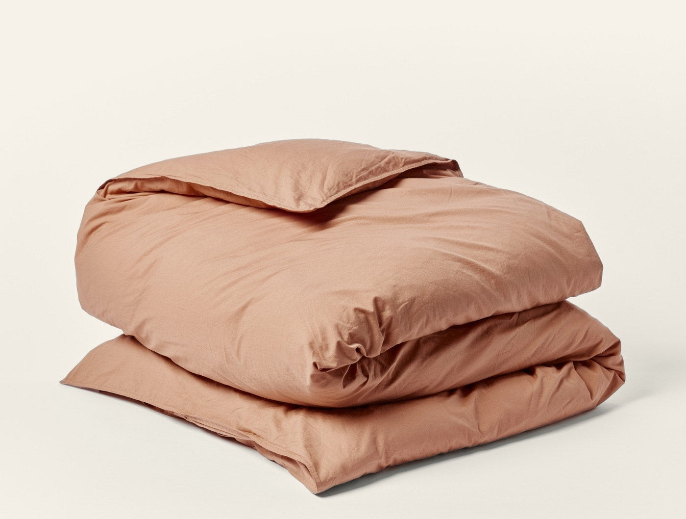 Coyuchi Crinkled Percale duvet cover folded, shown in warm terracotta, textured percale fabric.